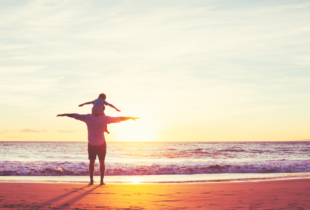 Person standing with child on his shoulders at Guernsey beach - Representing personal trust solutions from an independent financial services provider